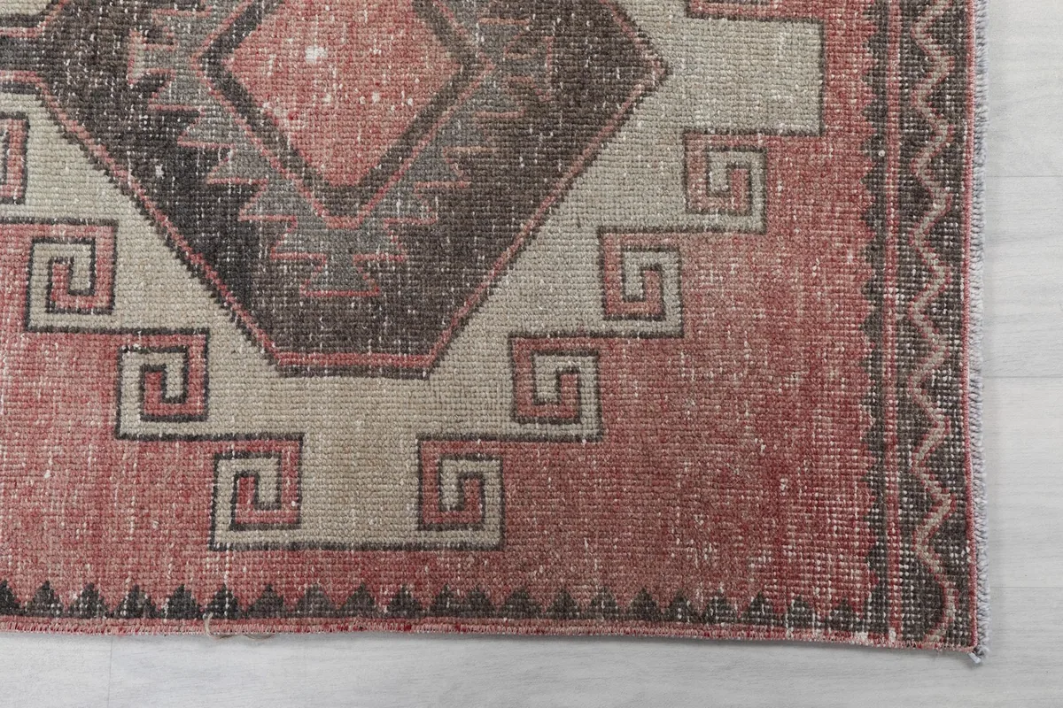 Detailed view of the rug's corner, showing geometric shapes and the faded rose and black colors.
