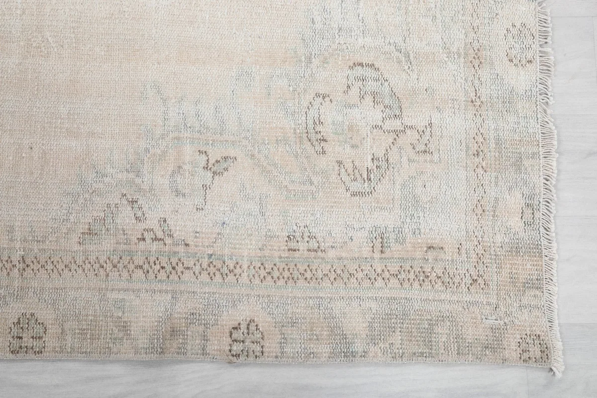 Detailed view of the corner motif and border design on the cream vintage rug, showing muted gray and beige tones.