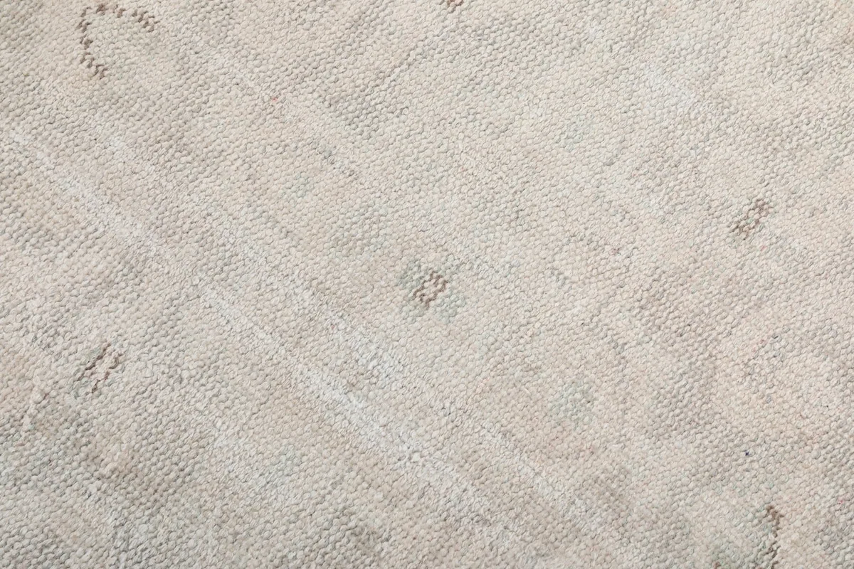 Texture shot showing the low wool pile of the vintage cream rug with subtle color variations.