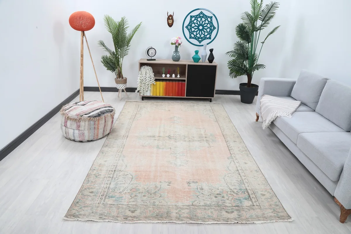 Vintage pink and blue Anatolian rug displayed in a living room setting with a sofa and plants.