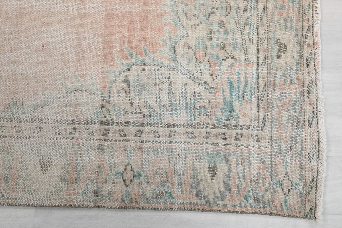 Close-up detail of the rug's border with faded blue and beige floral patterns.