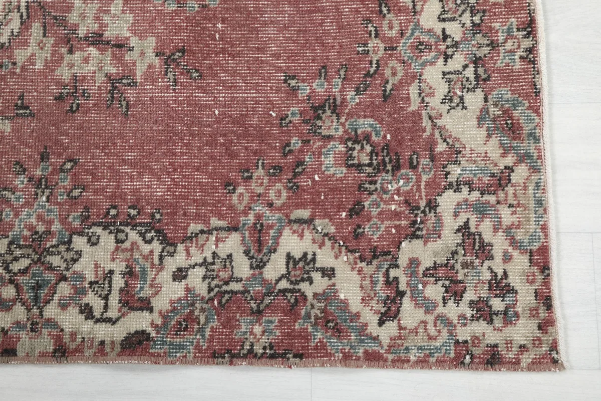 Corner detail of the rug showing beige and gray floral motifs on a rose field.