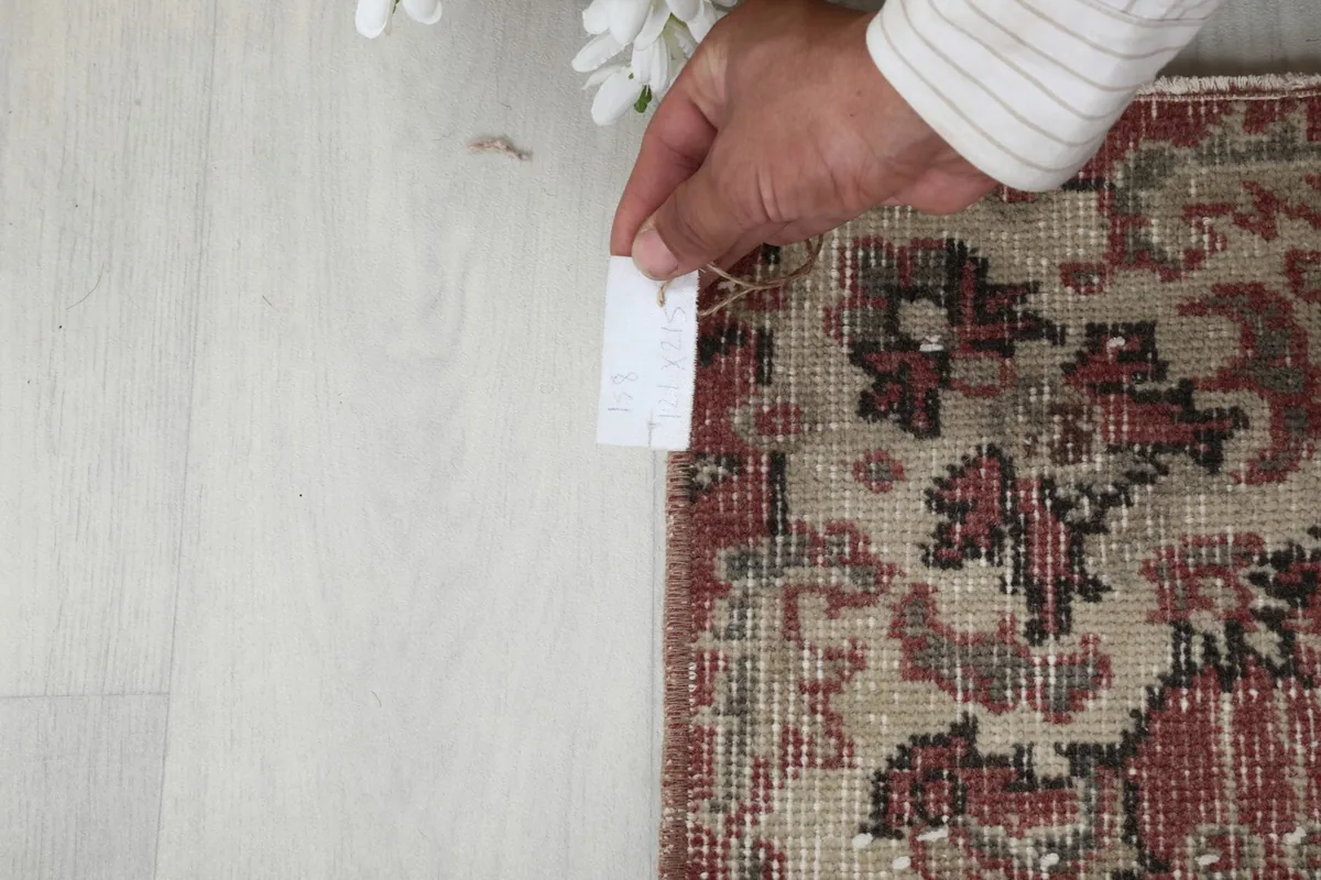 Hand holding a measurement tape next to the rug, indicating its size and scale.