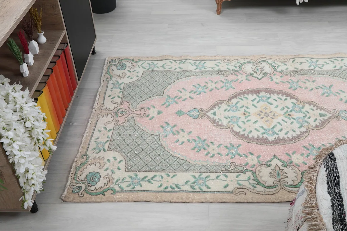 Angled view of the entire rug, showing its faded rose and green colors in a room setting