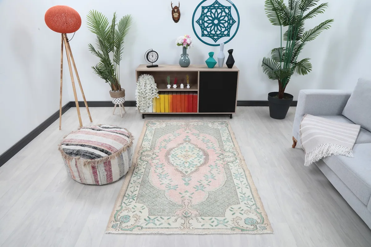 Vintage Anatolian rug with rose and green tones placed in a living room setting with a light gray couch