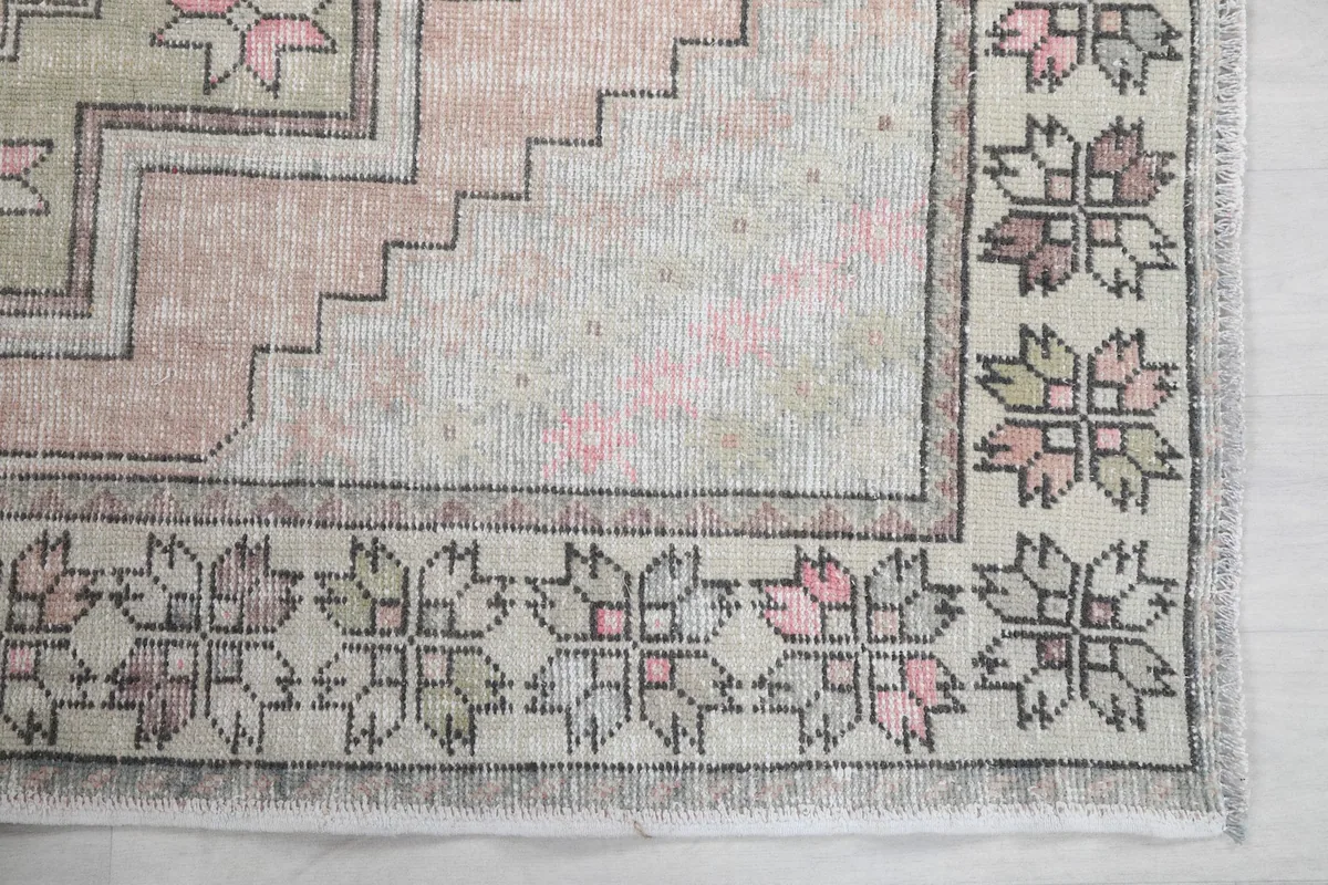 Detailed view of the rug's corner, highlighting the intricate geometric border design in gray and pink.