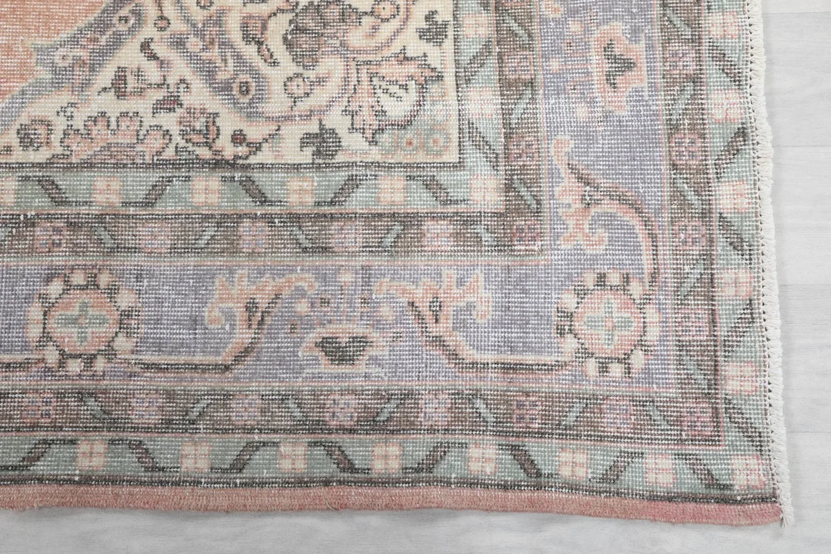 Detailed view of the intricate gray and green border patterns of the vintage rug.