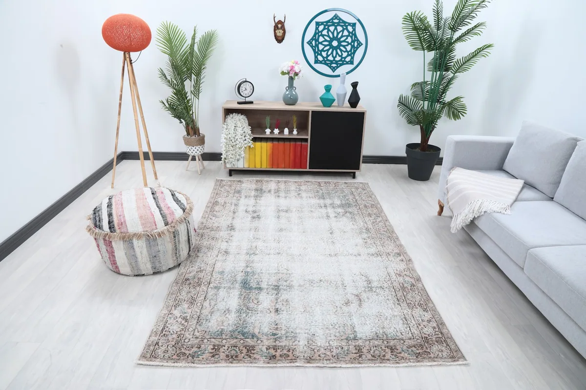 Vintage Anatolian rug displayed in a modern living room setting with a gray sofa and striped ottoman.