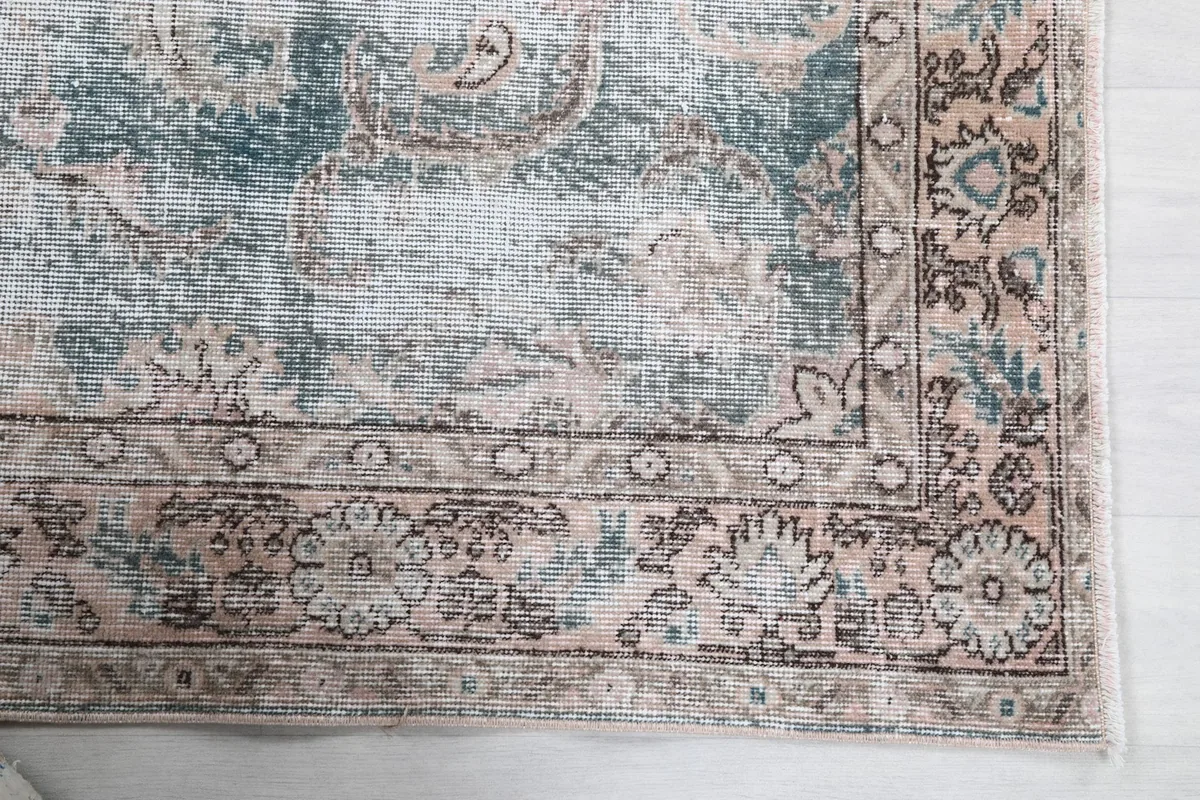 Close-up detail of the rug's border showing faded rust and blue floral and geometric patterns.