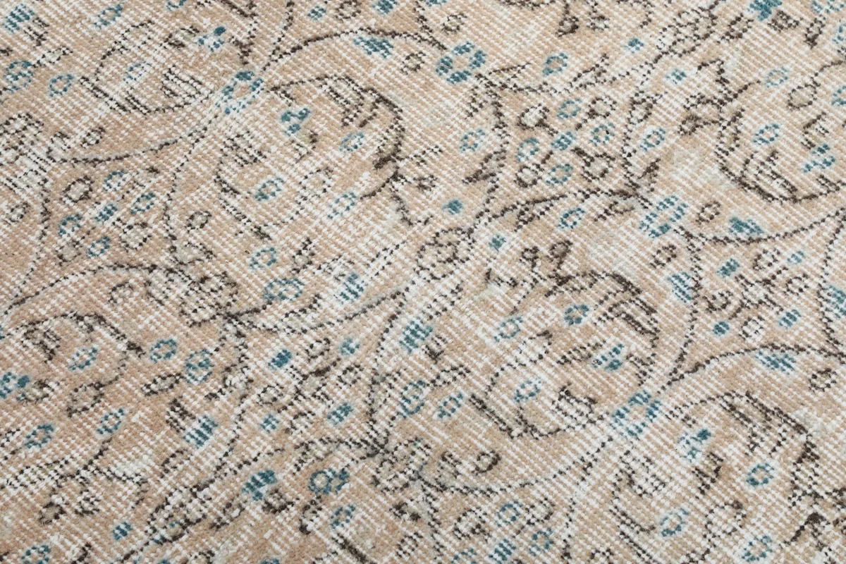 Close-up detail of the floral and geometric patterns in blue and brown on the beige rug