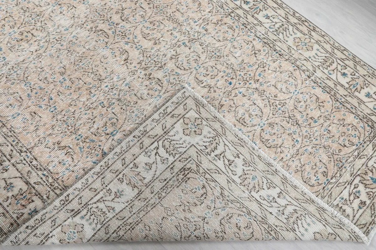 Corner of the beige and blue vintage Anatolian rug folded to show the hand-knotted back