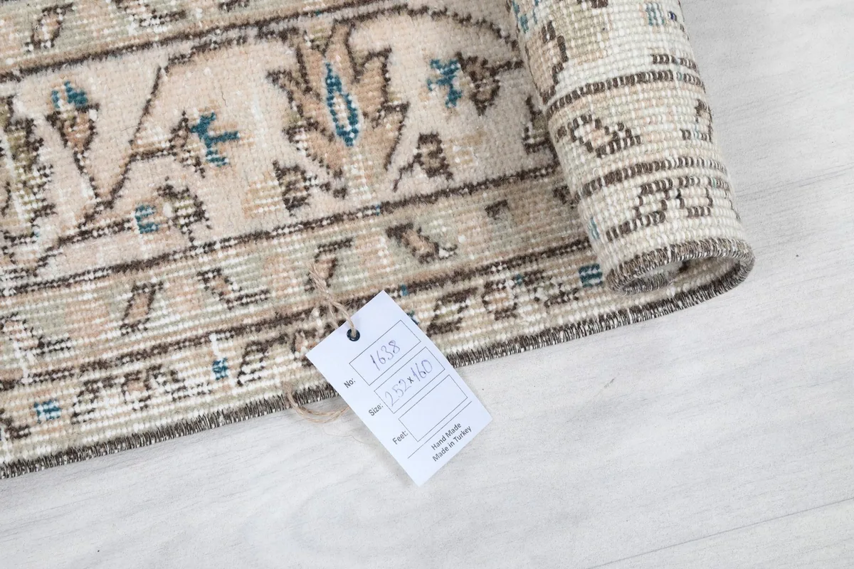 Rolled edge of the beige and blue vintage Anatolian rug with a product tag showing measurements