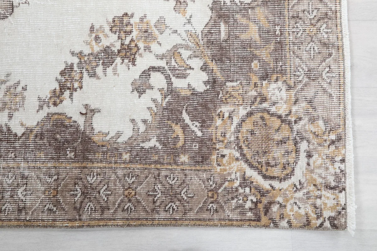 Detailed view of the rug's border pattern, showing geometric motifs in brown and beige with subtle wear.