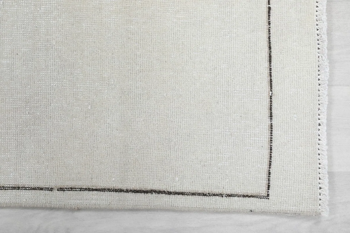 Detail of the subtle gray border and the edge of the hand-knotted wool pile rug.