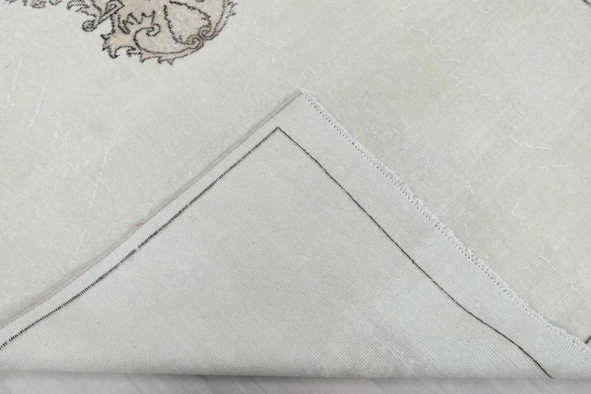Underside of the rug revealed by a fold, showing the cotton foundation and hand-knotted construction.