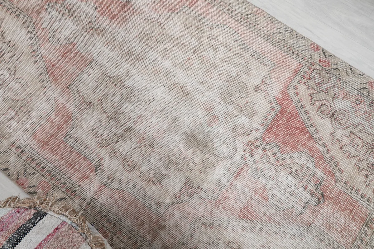 Angled close-up showing the vintage patina and subtle rose tones of the rug