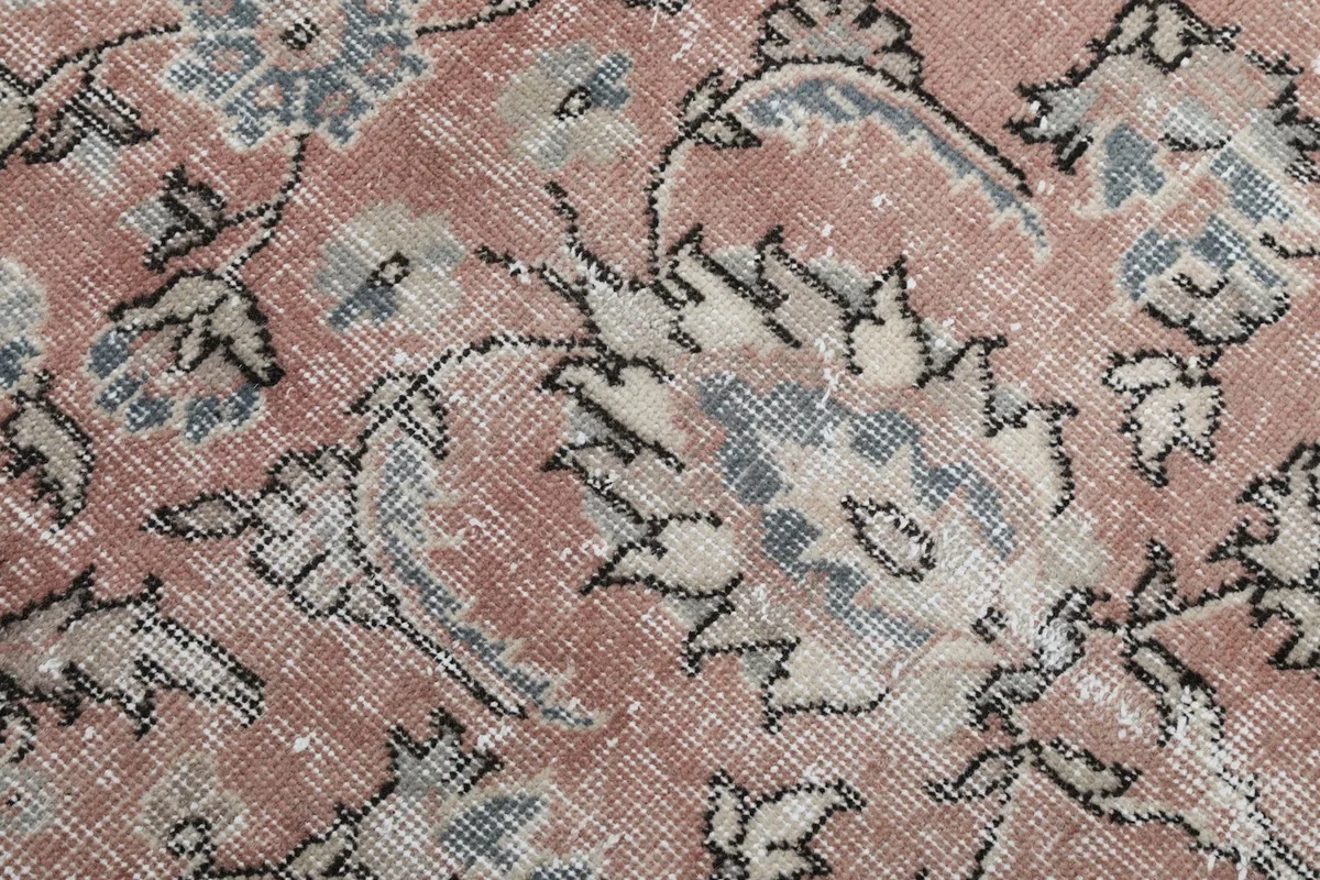Macro detail of the low wool pile, hand-knotted texture, and faded rose and gray colors