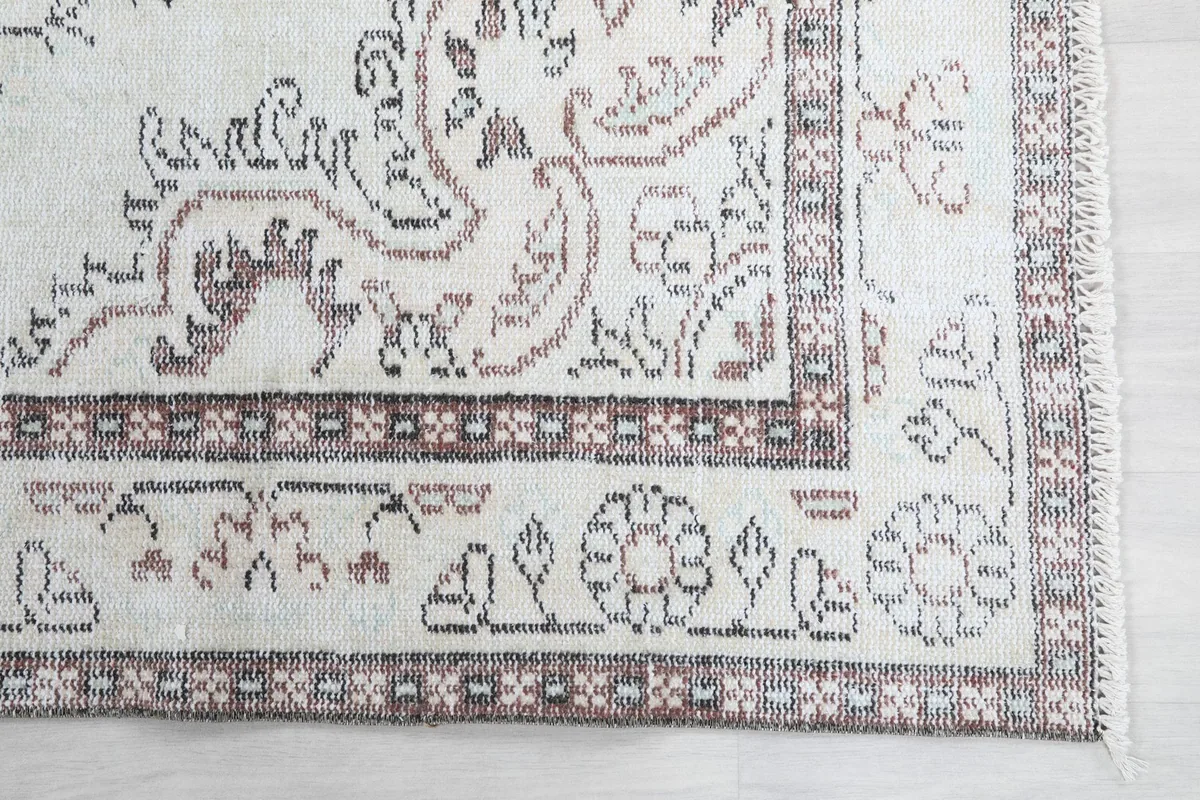 Detailed view of the rug's border pattern, showing brown and tan colors against the cream.