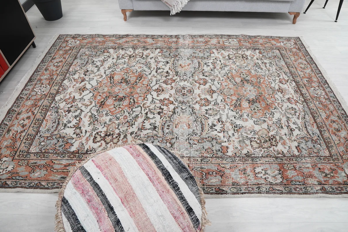 Cream Orange Floral Anatolian Rug with a pouf in the foreground, demonstrating its size in a room.