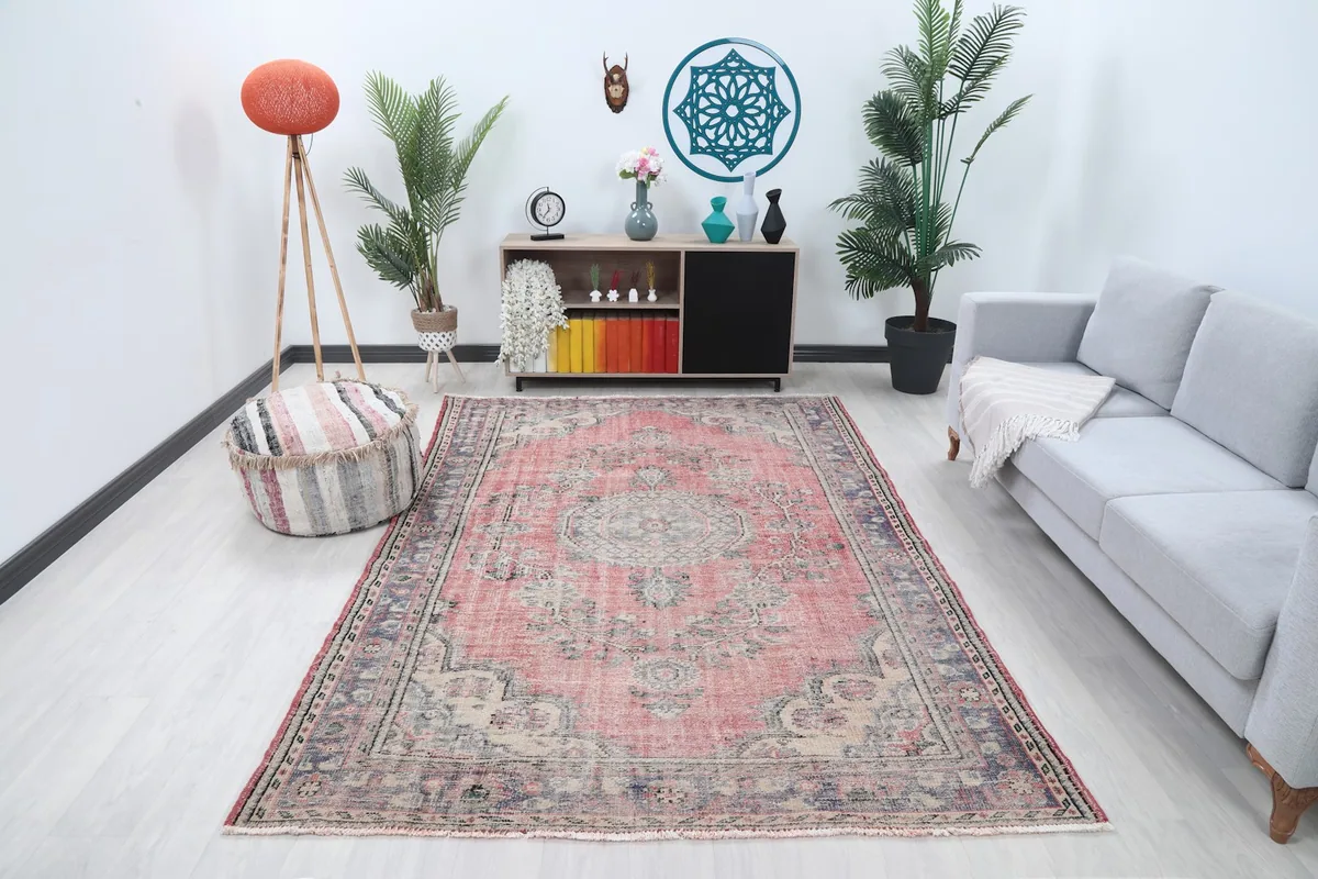 Rose and beige vintage rug in a living room setting with a gray sofa and wooden cabinet