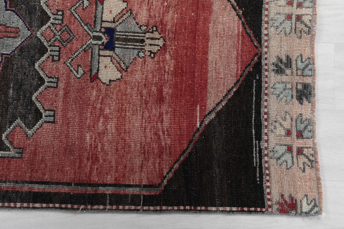 Detailed view of the rug's corner, showing the rust field, gray border, and beige fringe pattern