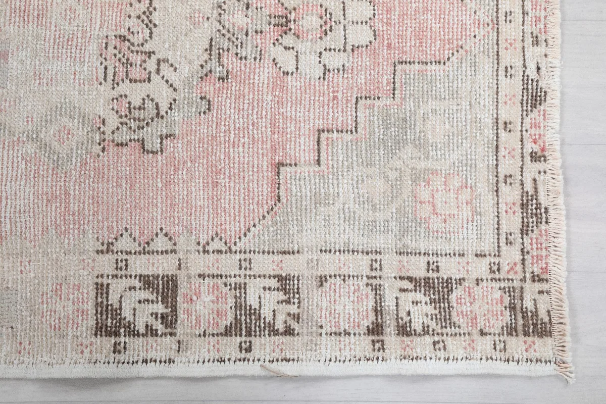 Detailed shot of the rug's end, showing a geometric border design and faded colors.
