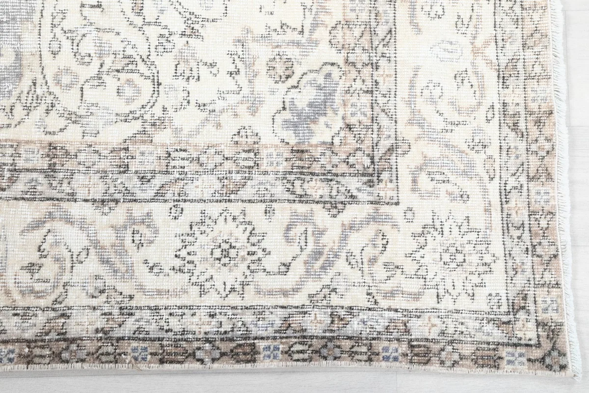 Detail of the rug's corner, highlighting the intricate ivory and tan floral border motifs.