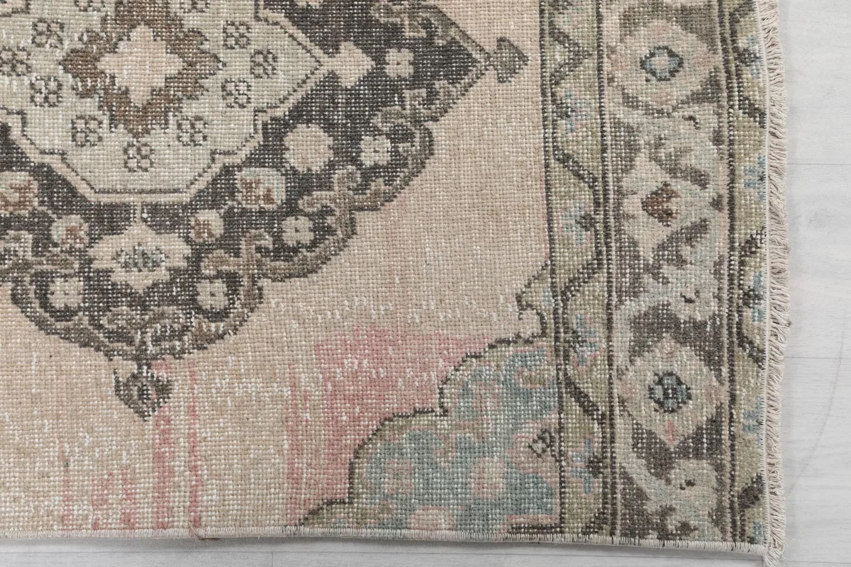 Detailed view of the rug's border and a faded pink medallion with blue accents.