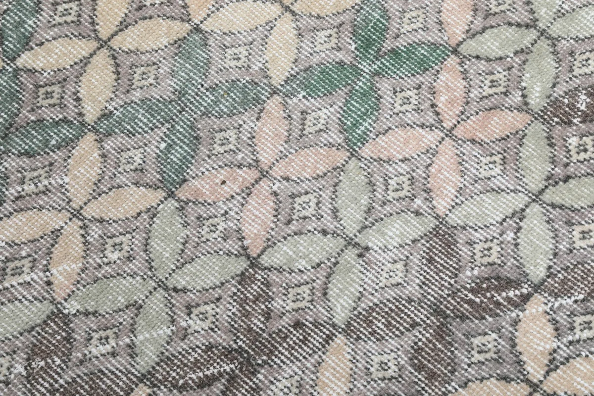 Close-up of the hand-knotted wool pile showing the intricate gray, pink, and green geometric motifs