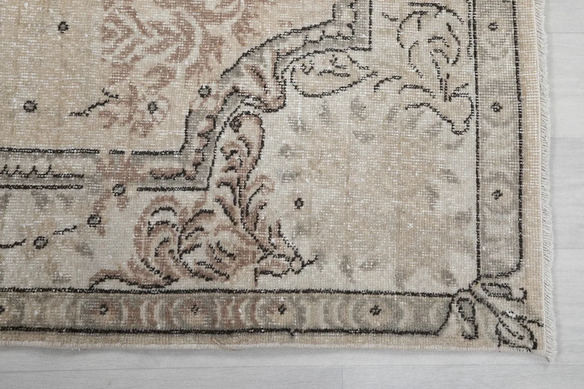 Detailed view of the rug's border design and corner, showing faded charcoal and rose tones