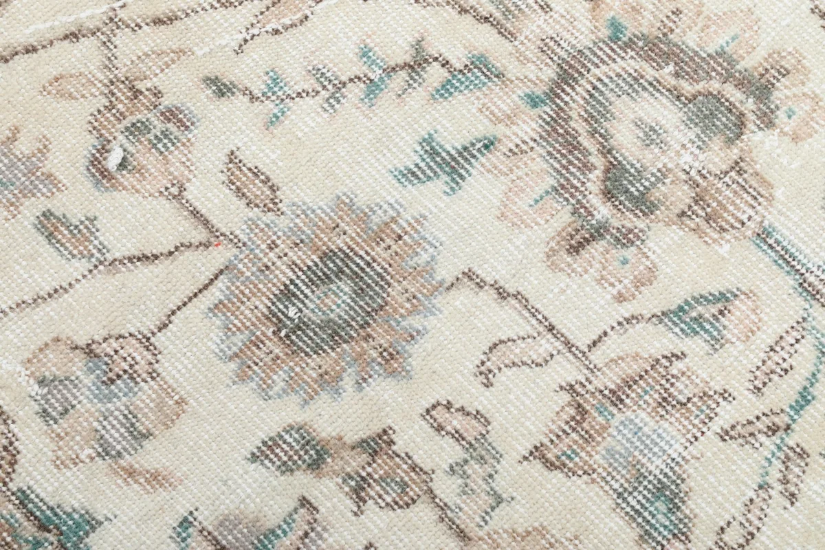 Close-up of the faded blue and tan floral details and the low pile texture of the rug