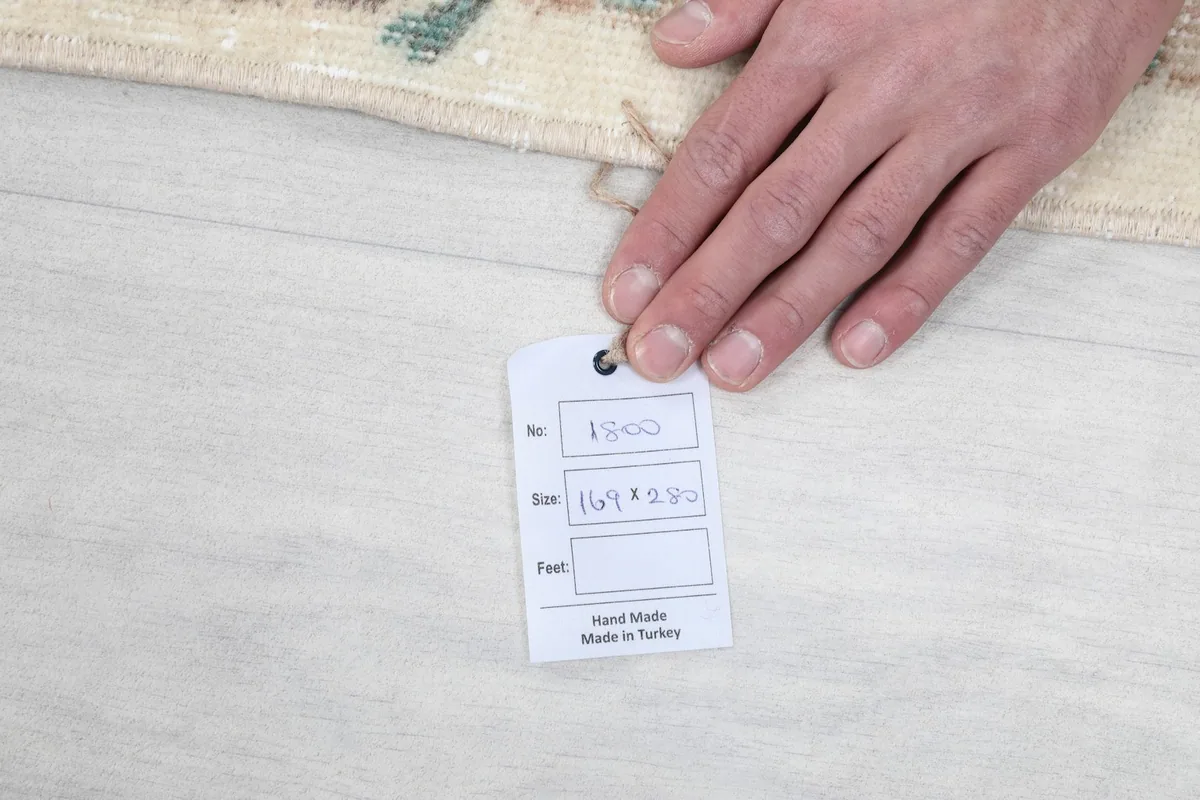 Hand holding a tag indicating the rug's hand-made origin and size in centimeters