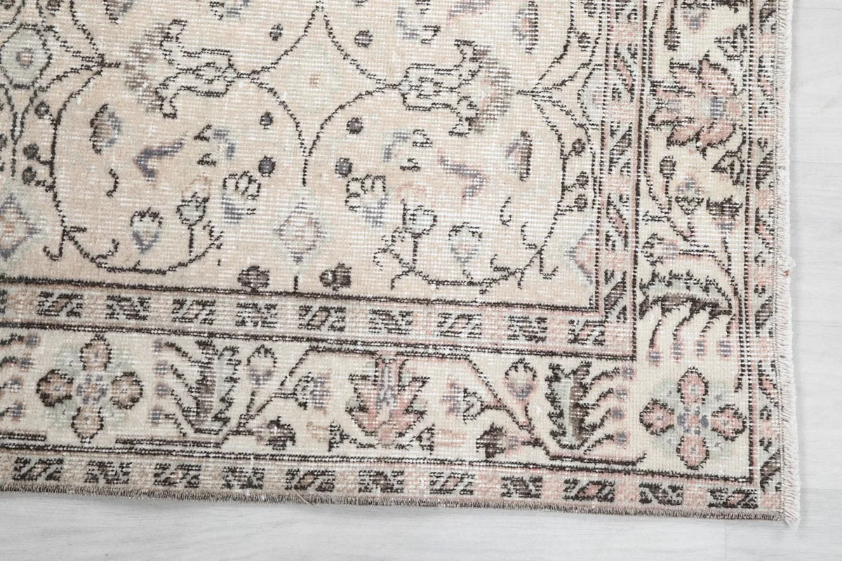 Detailed view of the rug's corner, showing the faded rose and gray floral motifs within the border.