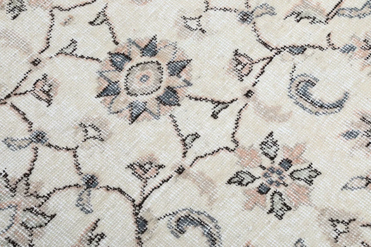 Extreme close-up of the floral motifs and wool pile texture in cream, rose, and gray tones