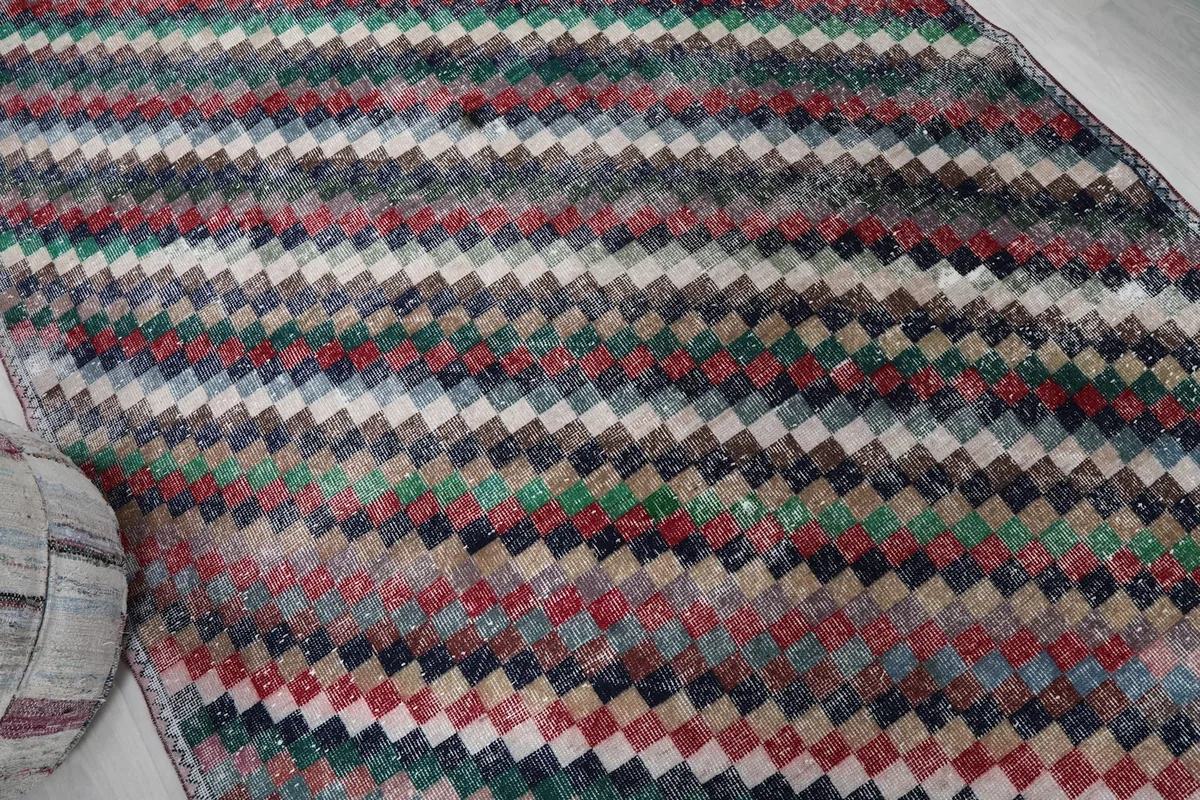 View across the rug, highlighting the diagonal lines formed by the multicolored squares and patina