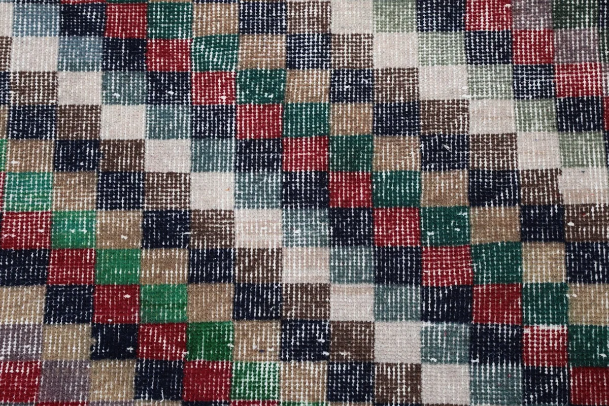 Close-up detail of the individual colorful squares and the wool pile on the vintage area rug