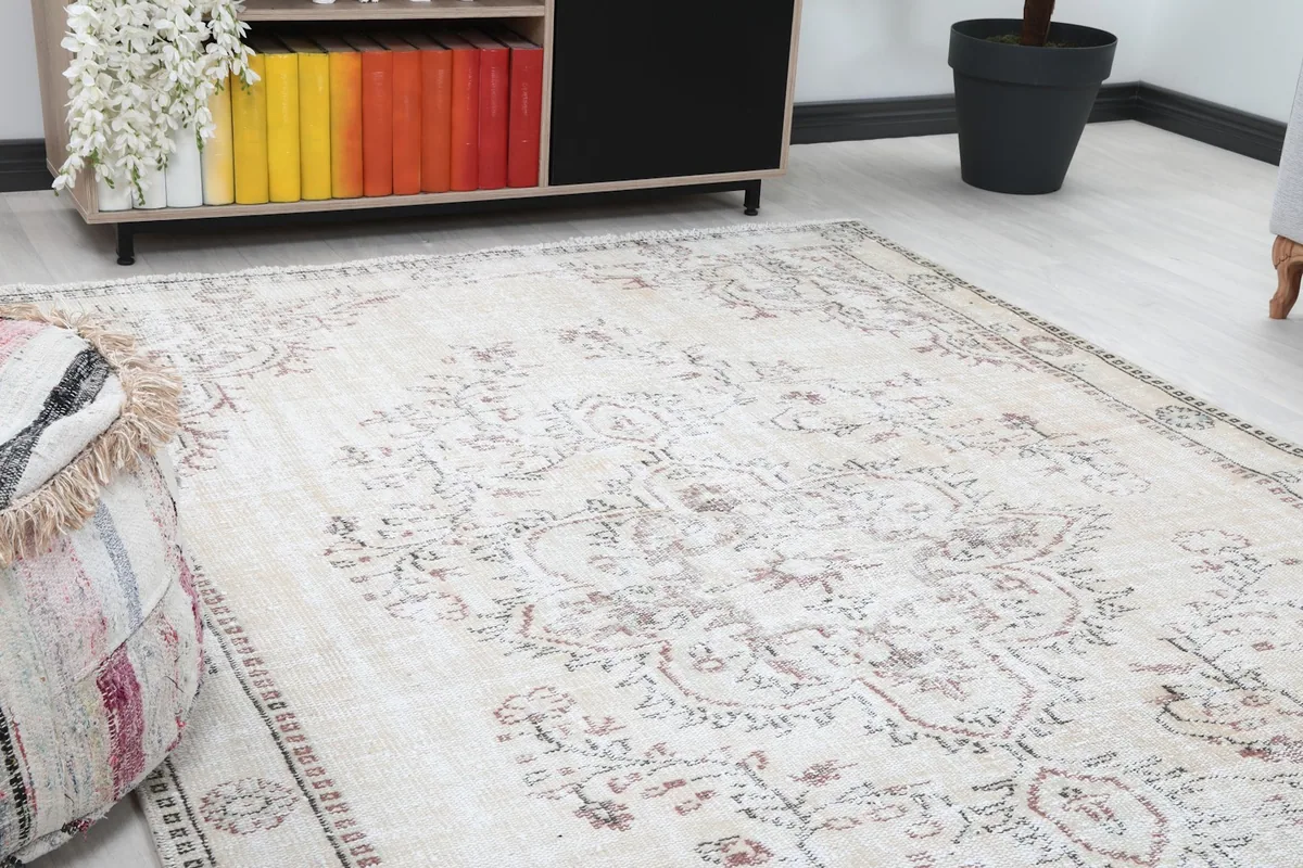 Close-up angle shot of the rug's ivory field and faded rose floral designs next to an ottoman