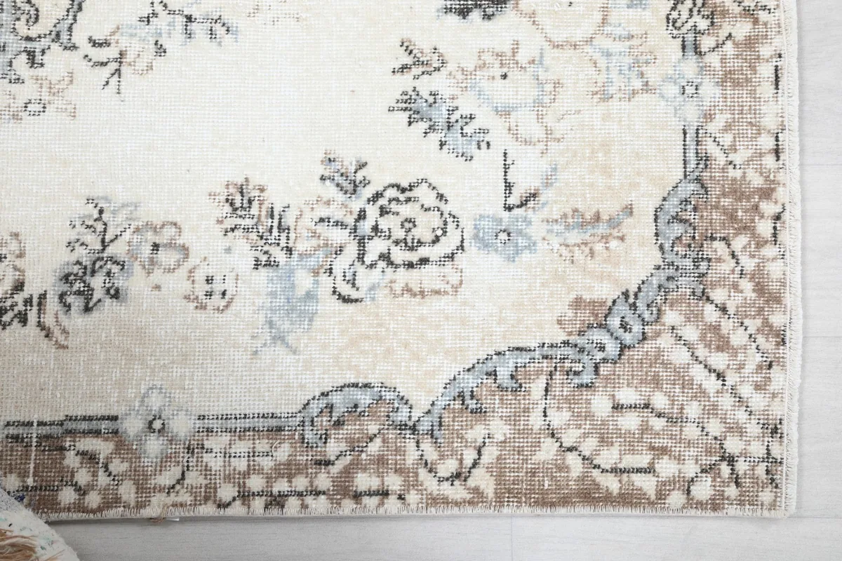 Close-up of the rug's corner showing the brown border and faded floral motifs in ivory and gray