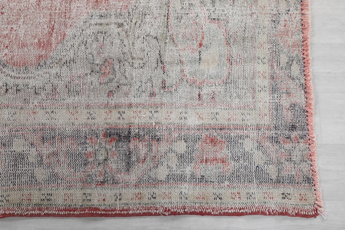 Detail of the rug's border design, featuring gray and cream patterns with a rose fringe.