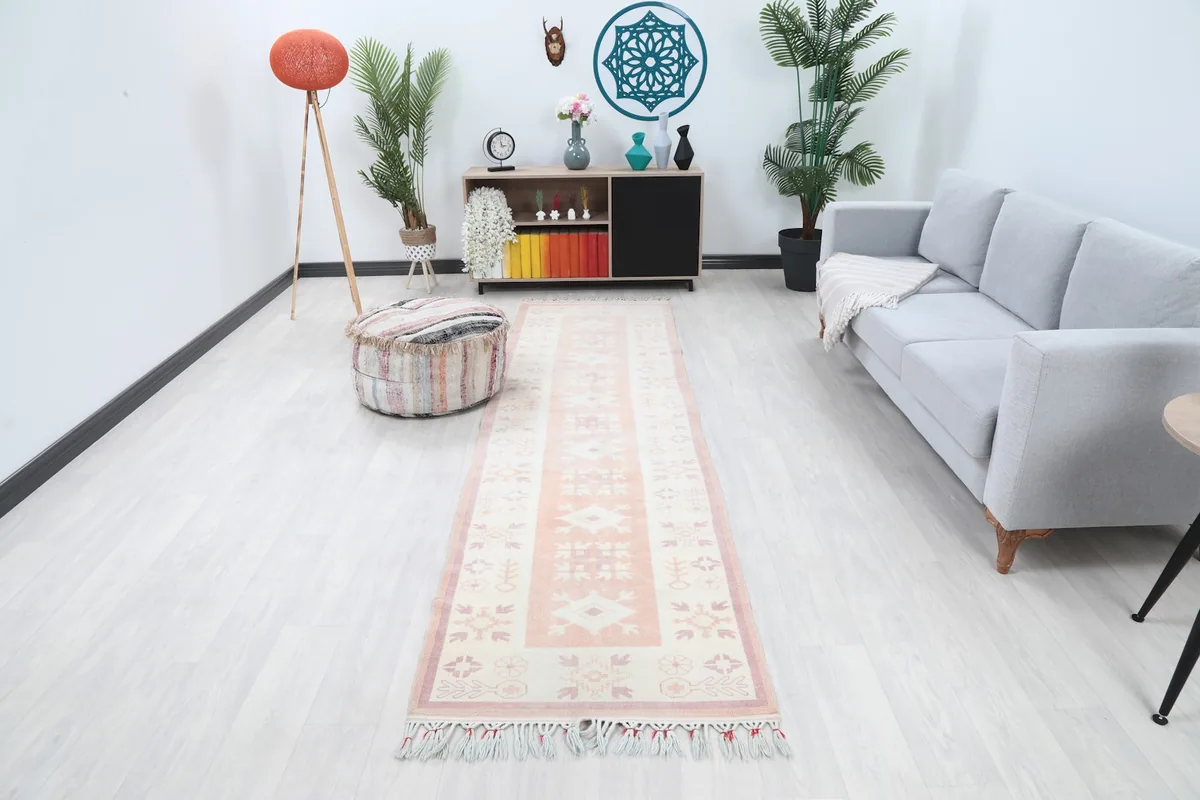 Rose and ivory geometric runner rug in a modern living room setting with a gray couch and light flooring.