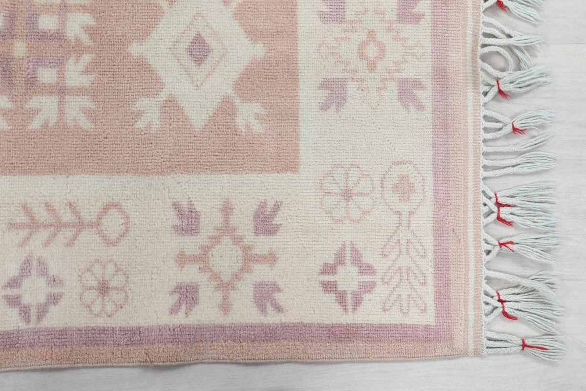 Close-up detail of the corner of the runner rug, showing geometric motifs in rose, ivory, and purple, with fringe.
