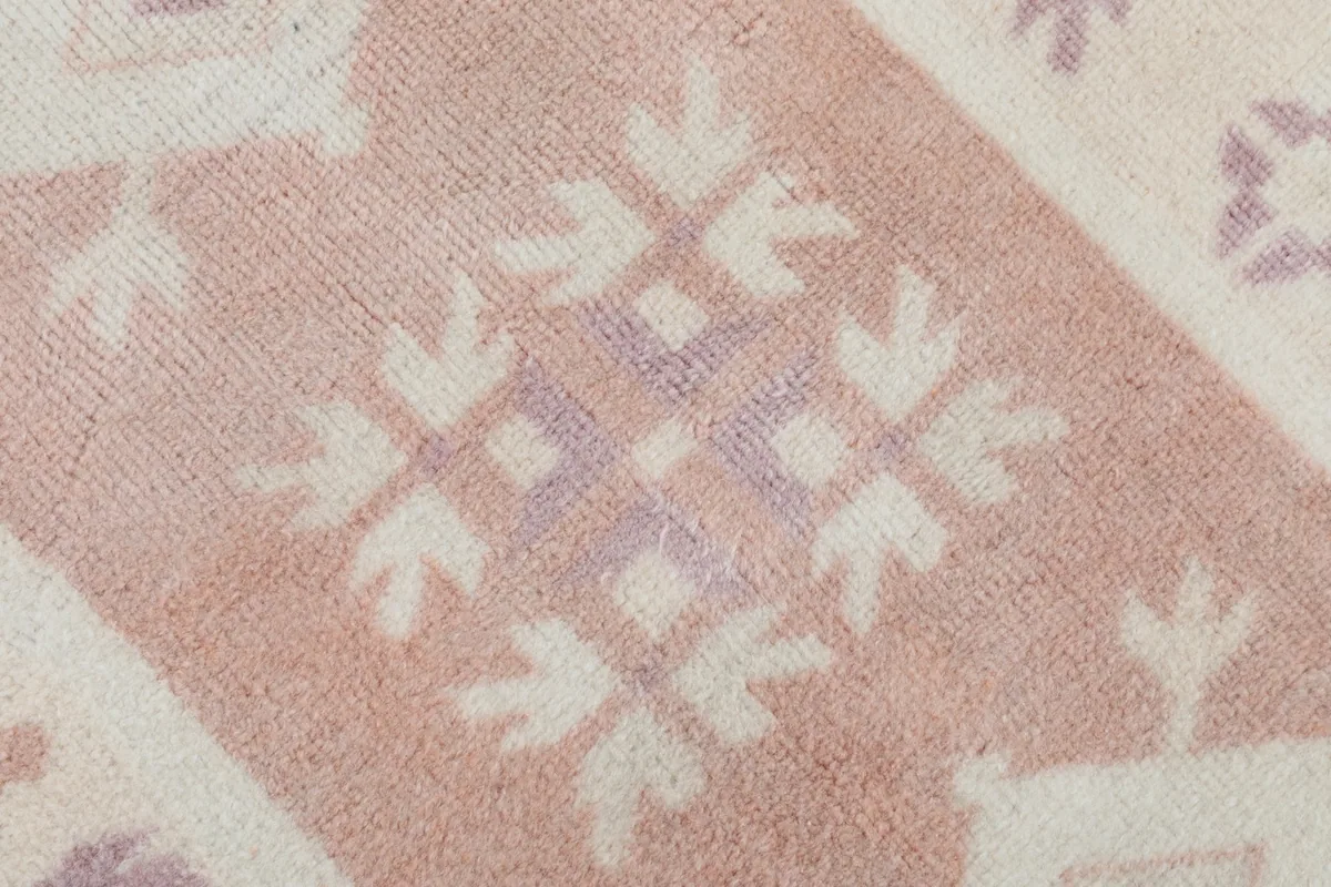 Detailed close-up of a specific geometric motif in rose and ivory within the rug's pattern.