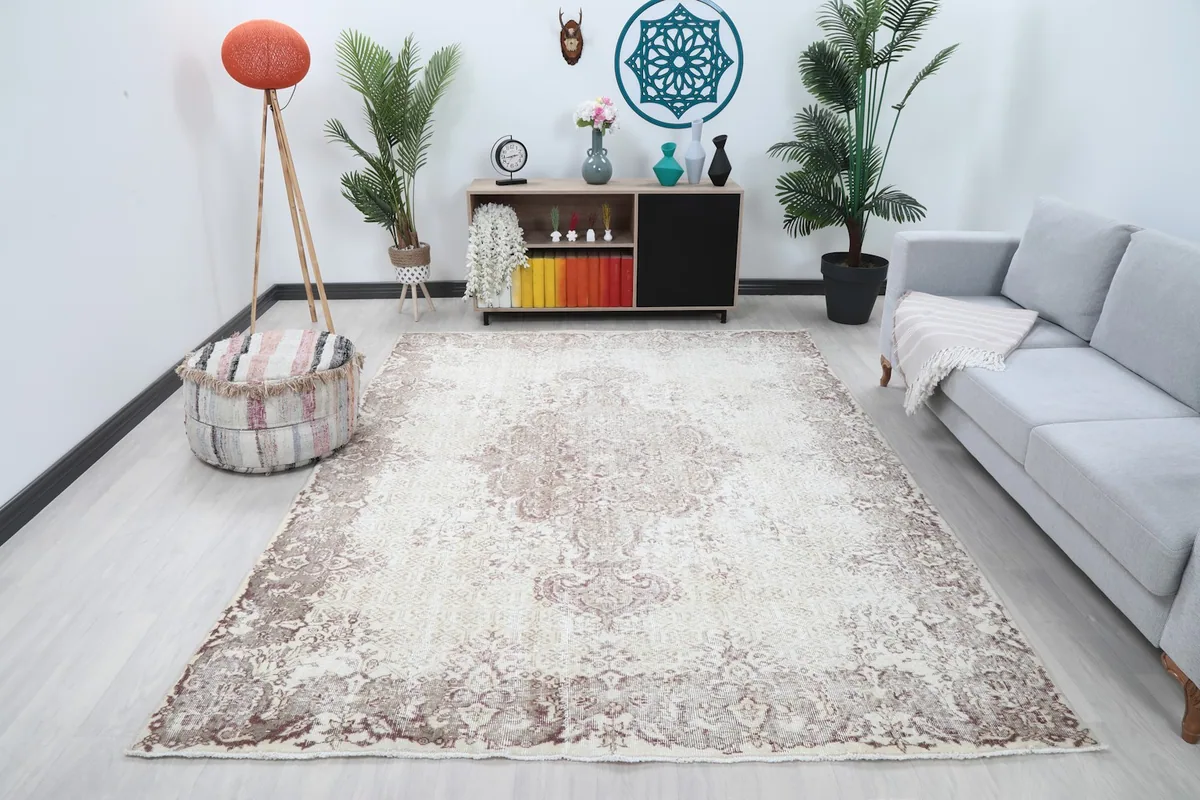 Ivory and rose vintage rug displayed in a living room setting with a sofa and plants