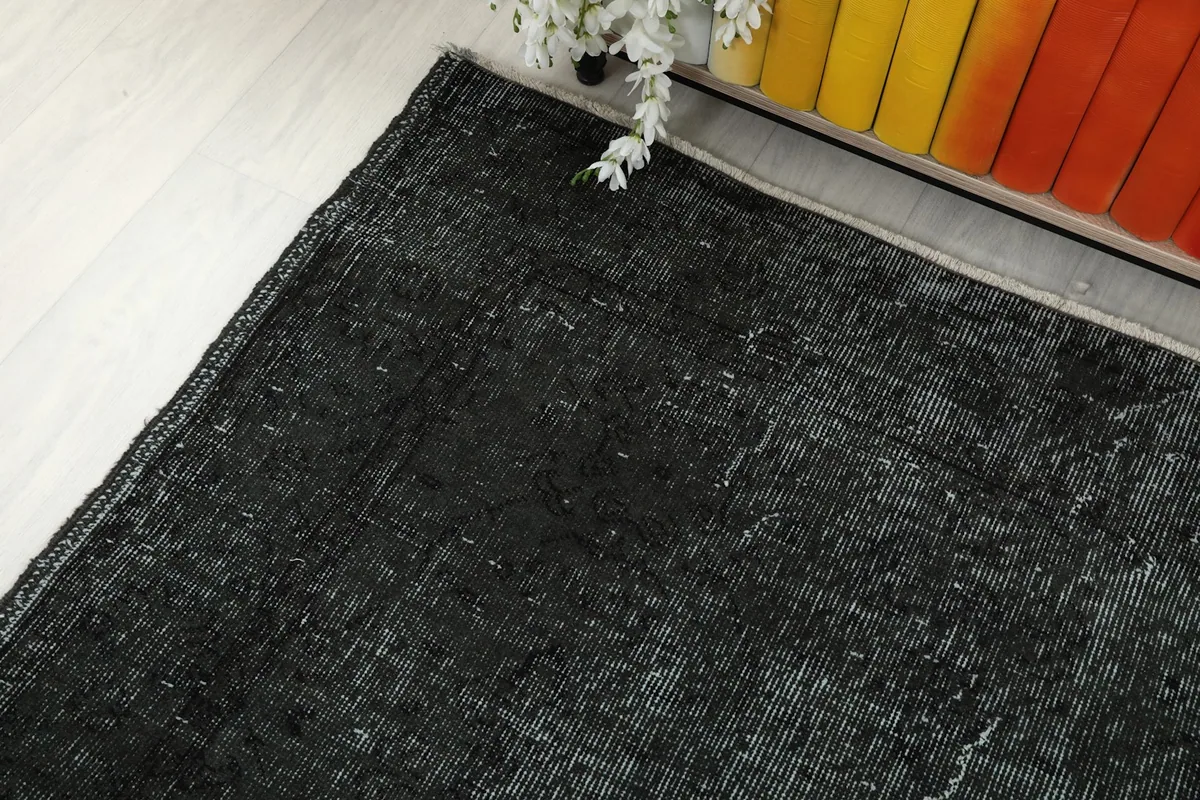 Corner view of the charcoal rug next to a wooden cabinet with colorful books.