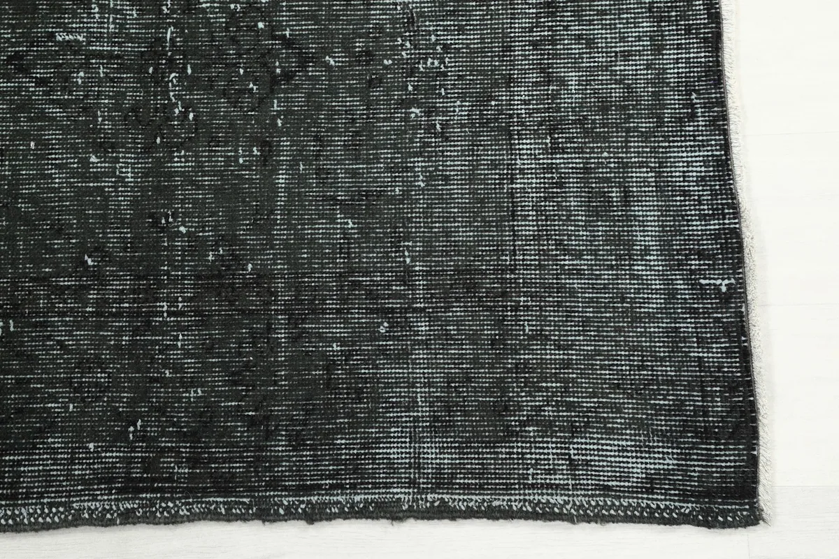 Detail of the rug's short fringe and edge, showing the charcoal and faded gray tones.