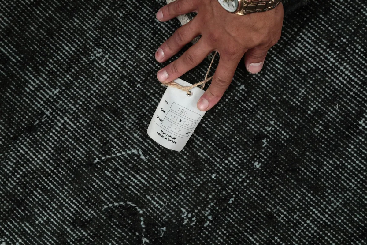 A hand holding a product tag on the rug's surface, indicating its origin and materials.