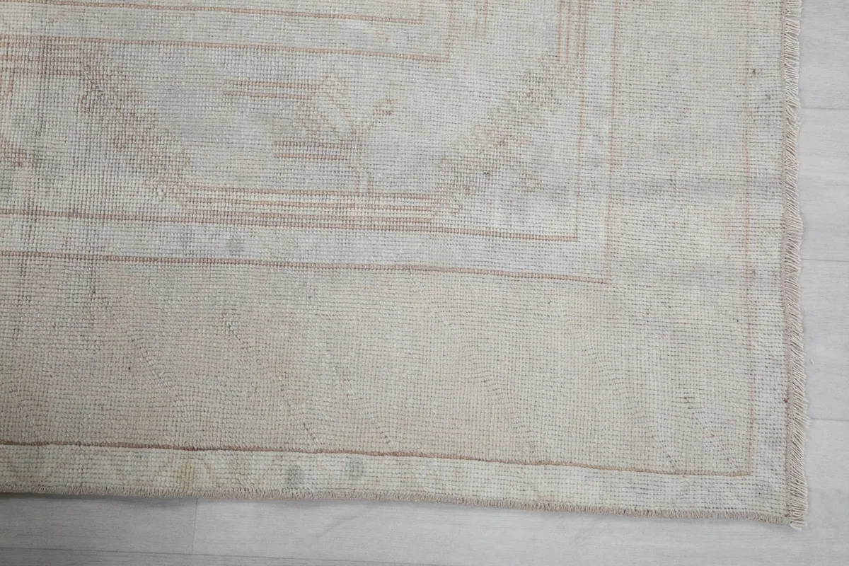 Detailed view of the rug's corner, showing the subtle geometric patterns and border in cream and beige.