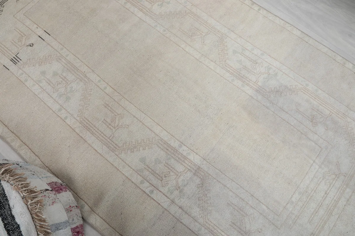 Overhead view showing the full length of the rug's cream field with faded geometric designs.