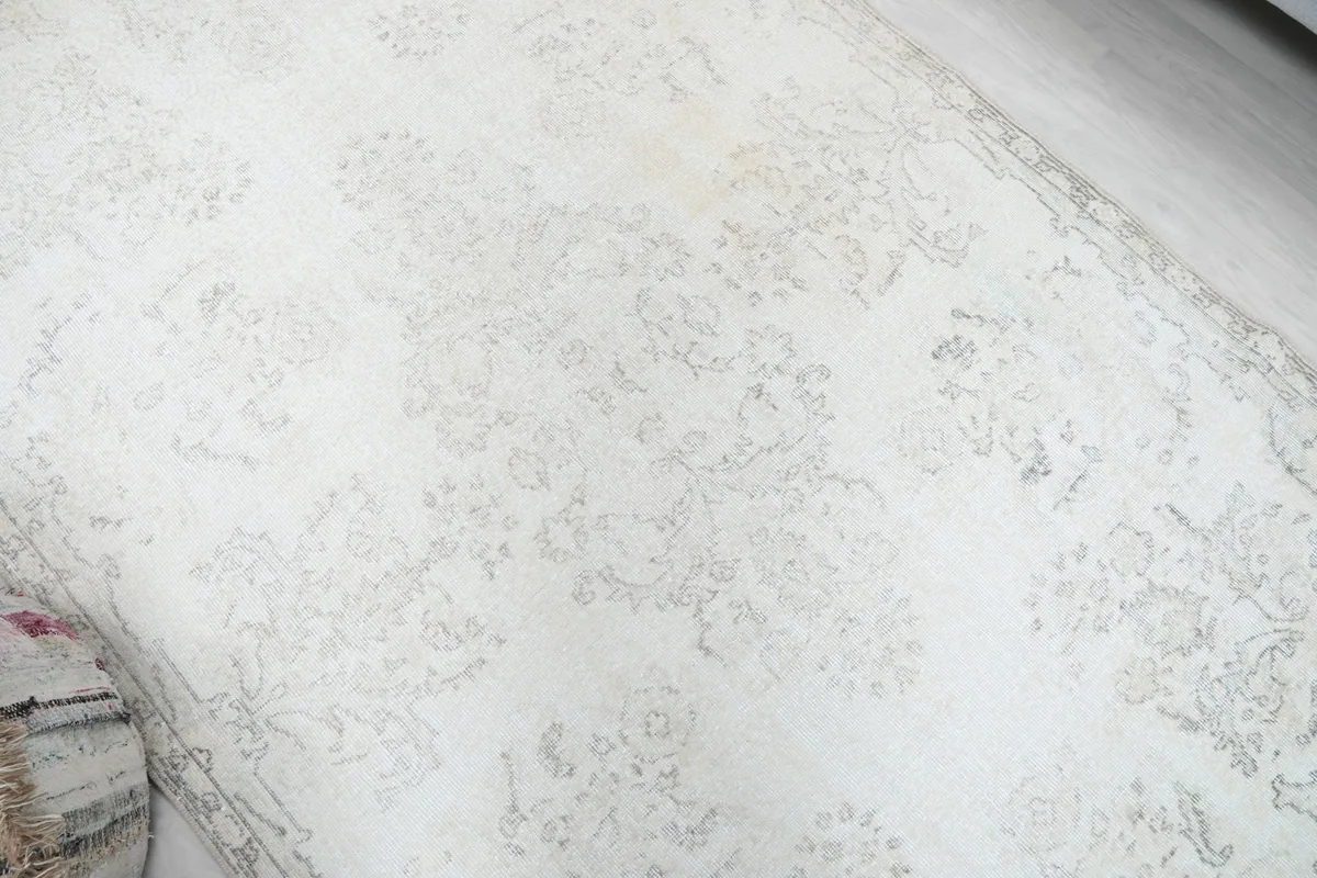 Diagonal view of the vintage rug, highlighting the soft cream field and distressed patterns