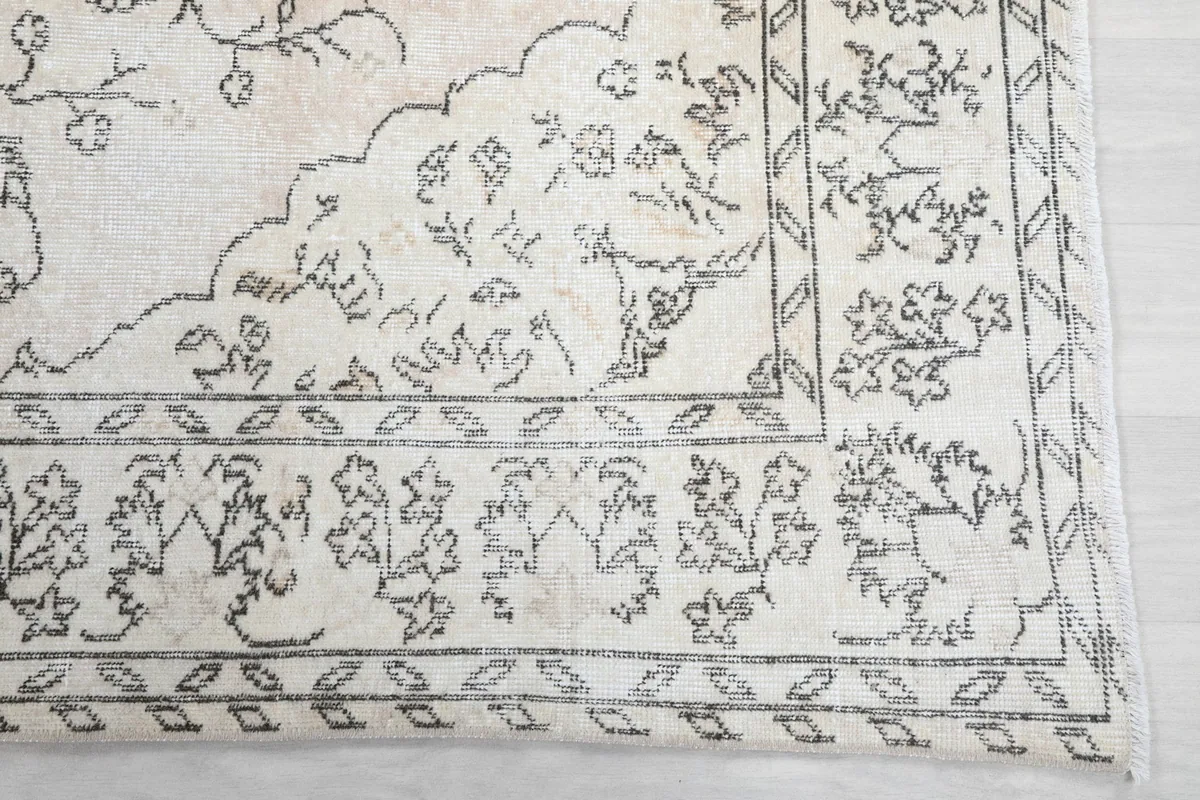 Detail of the rug's corner and border, highlighting the intricate charcoal floral design elements.